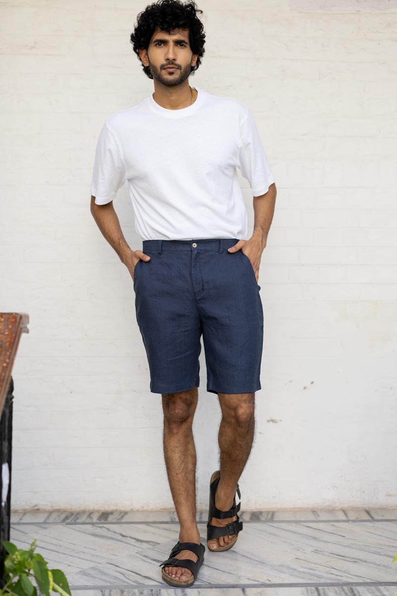 Man wearing a white t-shirt and Navy Blue Shorts standing against a white wall.