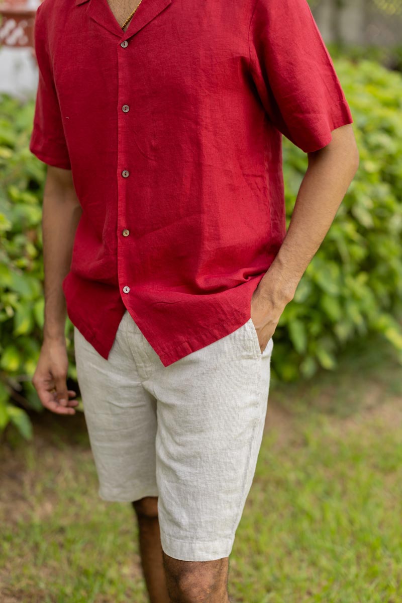 Person wearing a Cuban Collar Apple Red Shirt and beige shorts standing outdoors with greenery in the background