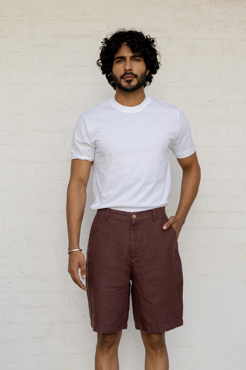 Man wearing a white t-shirt and Wine Shorts against a light brick wall.