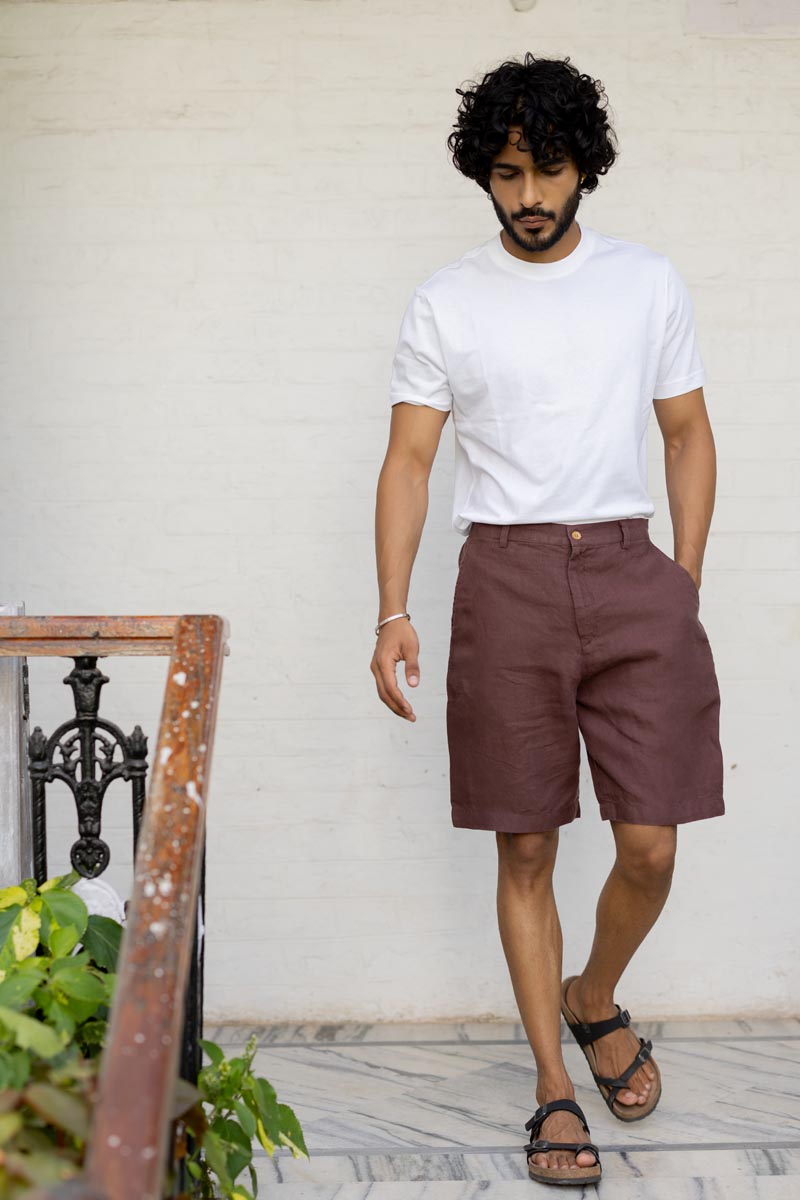 Man wearing a white t-shirt and Wine Shorts standing against a white wall.