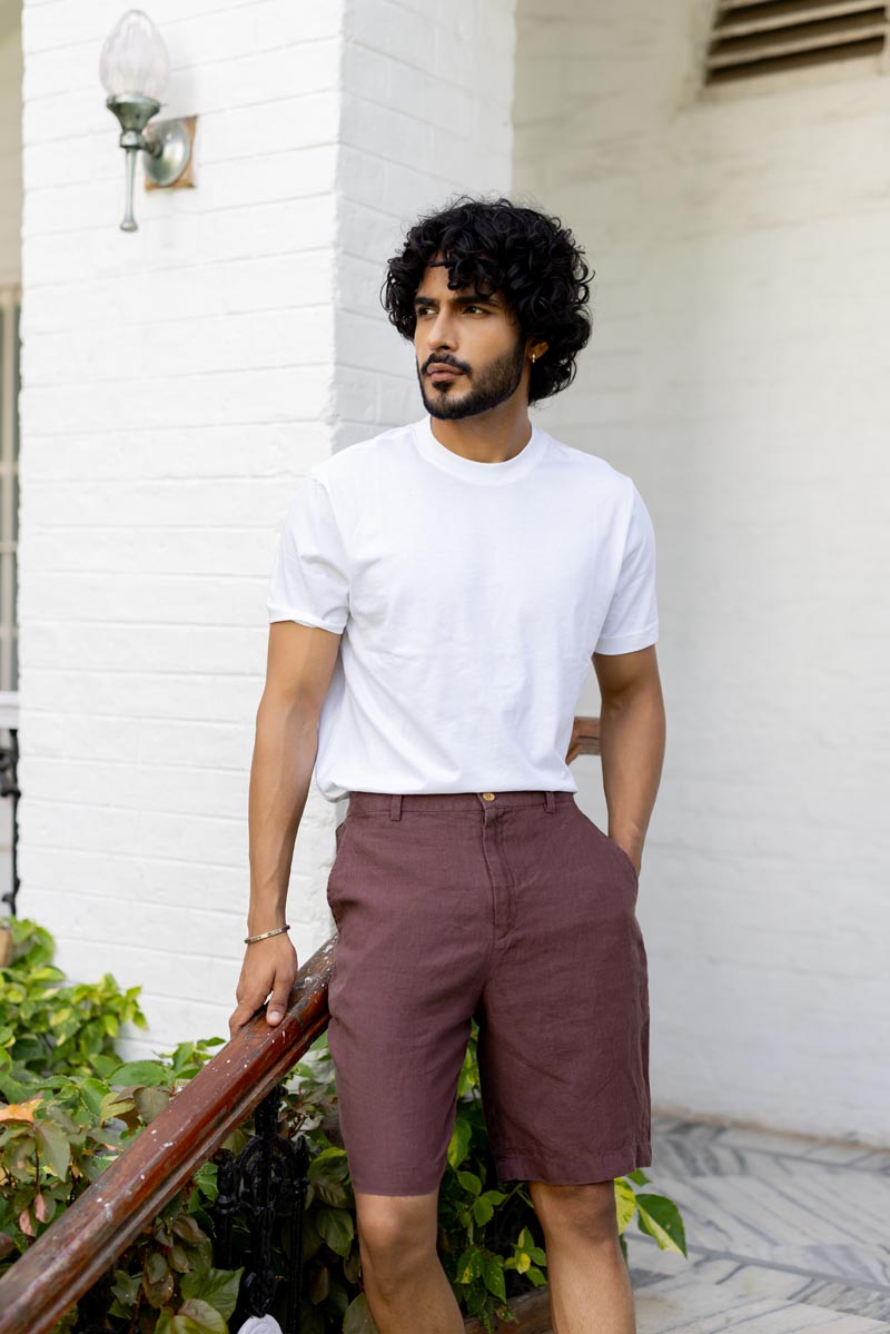 Man wearing a white t-shirt and Wine Shorts standing against a white wall.