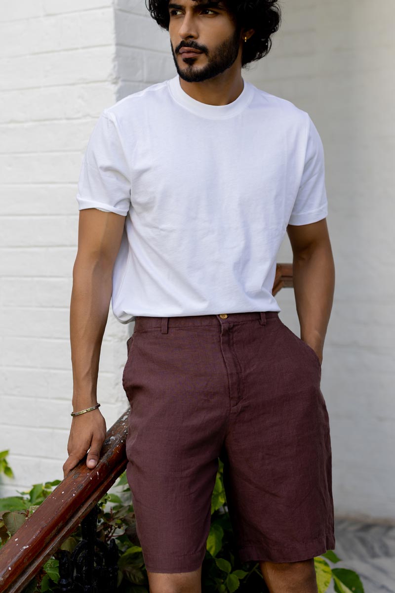 Man wearing a white t-shirt and Wine Shorts standing against a white wall.