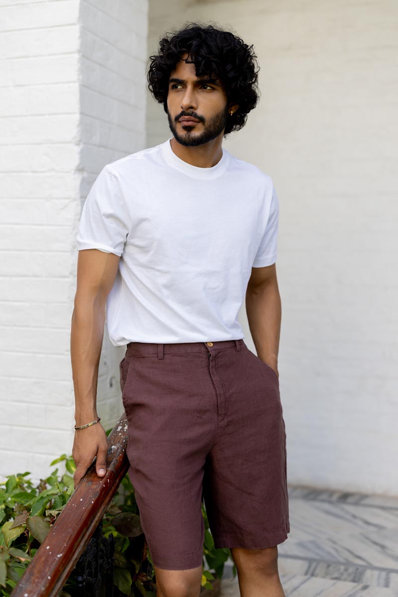 Man wearing a white t-shirt and Wine Shorts standing against a light-colored wall.
