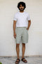 Man wearing a white t-shirt and Mint Green Shorts against a white brick wall.
