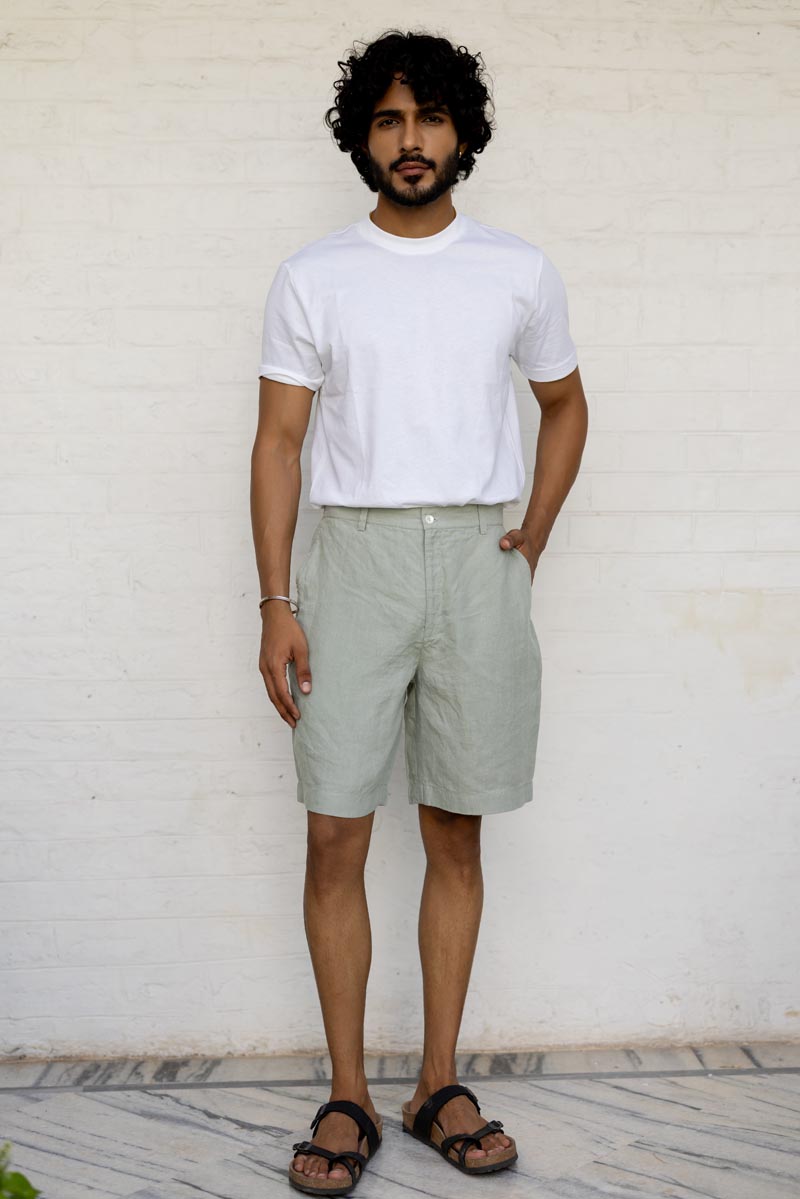 Man wearing a white t-shirt and Mint Green Shorts against a white brick wall.