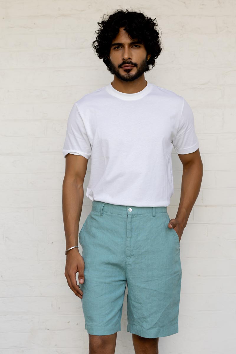 Man wearing a white t-shirt and Pine Green Shorts against a light brick wall.