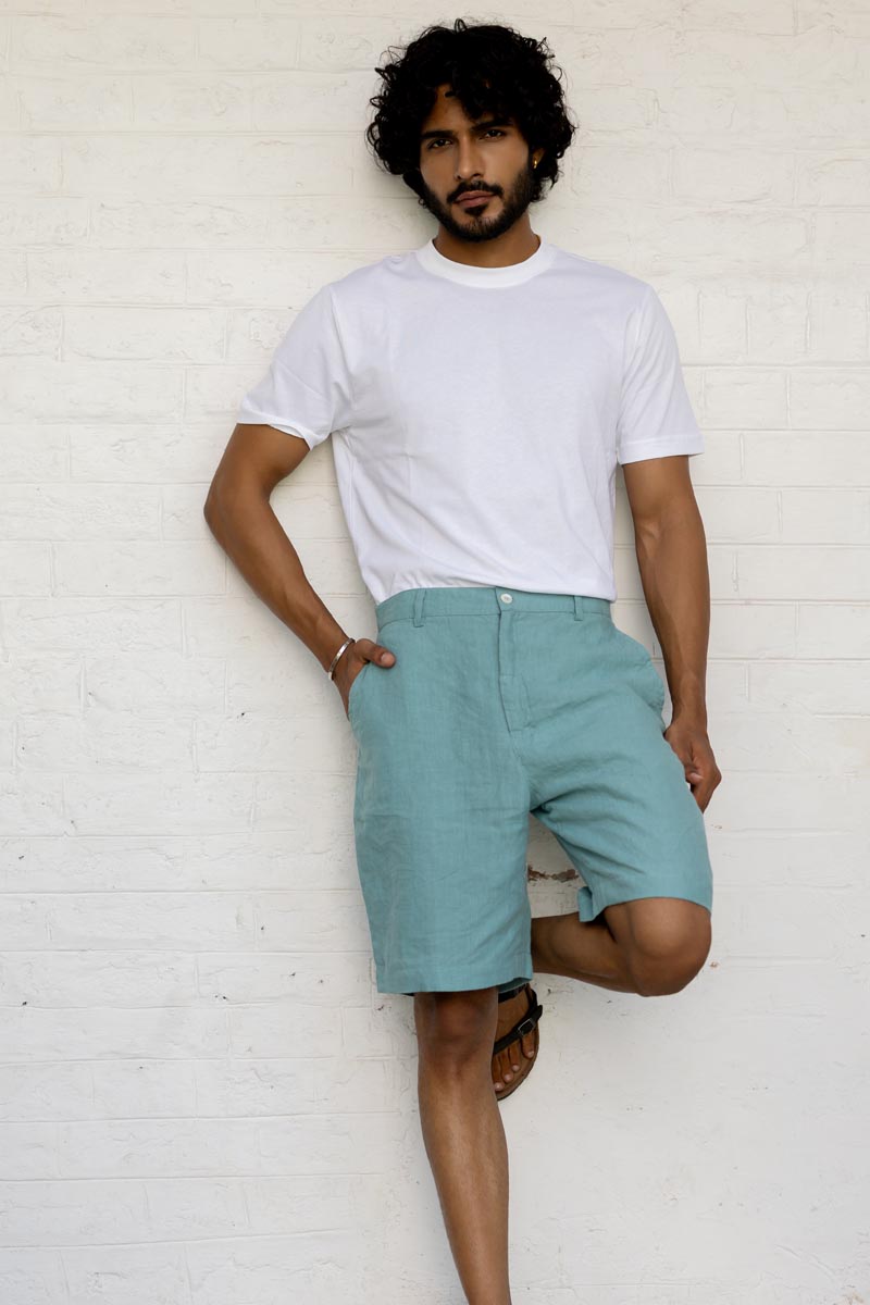 Man wearing a white t-shirt and Pine Green Shorts against a white brick wall.