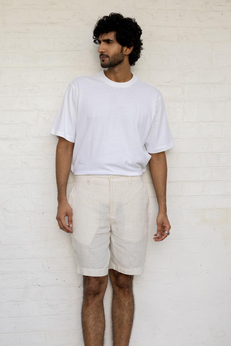 Man wearing a plain white t-shirt and Ivory Fine Stripe Shorts against a white brick wall.