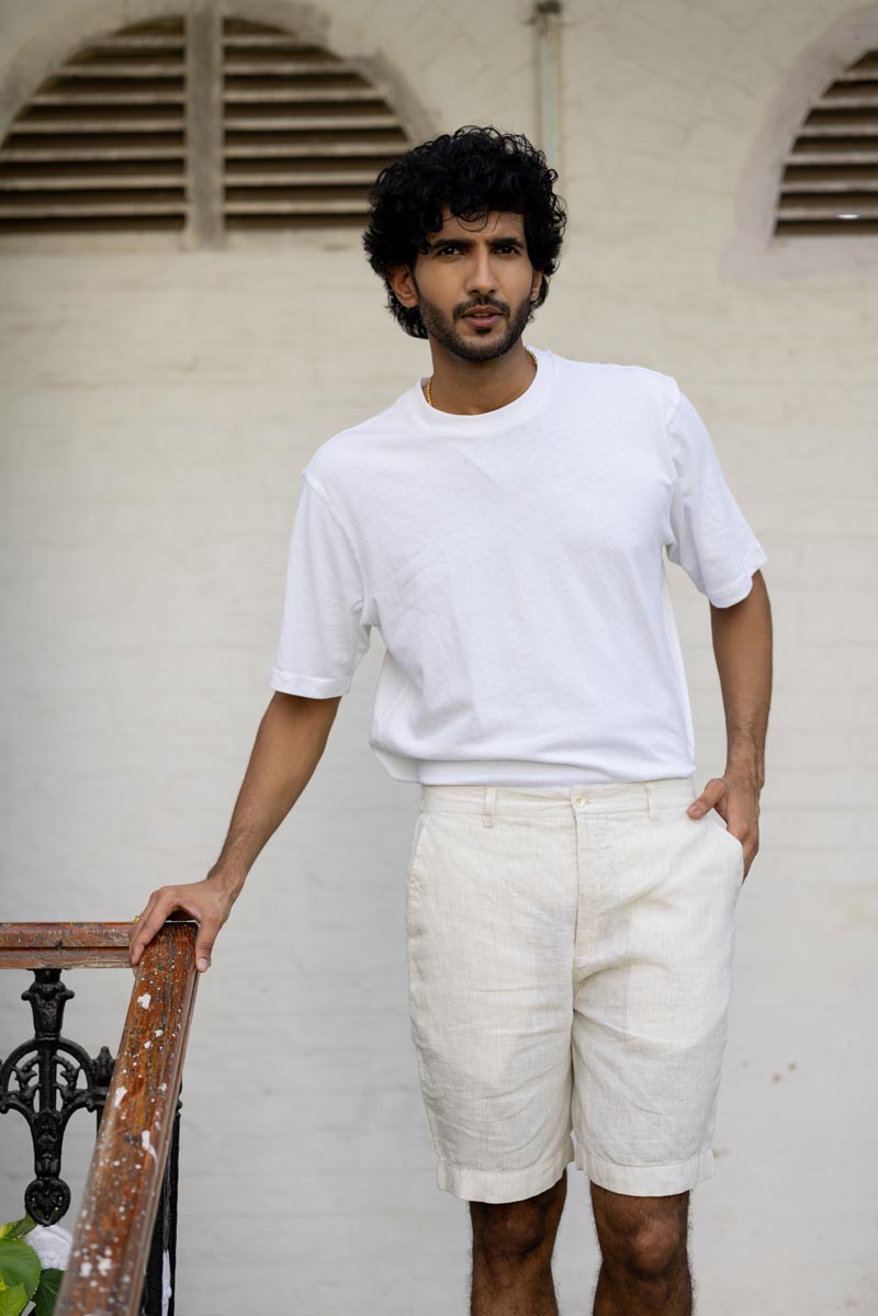 Man wearing a white t-shirt and Ivory Fine Stripe Shorts standing against a light-colored wall.