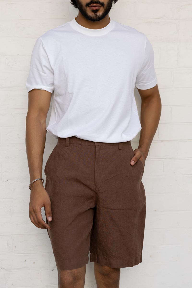 Person wearing a white t-shirt and Walnut Shorts against a white brick wall.