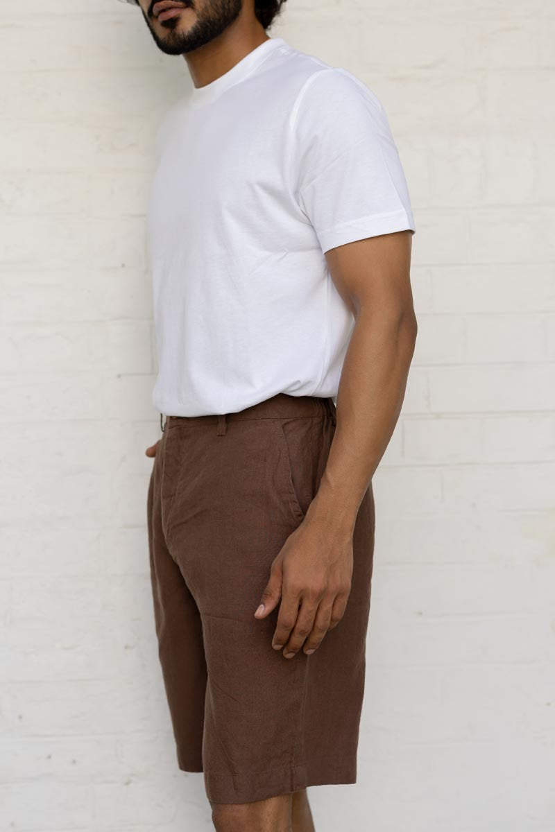 Person wearing a white t-shirt and Walnut Shorts against a white brick wall.