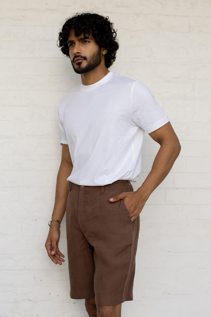 Man wearing a white t-shirt and Walnut Shorts against a white brick wall.