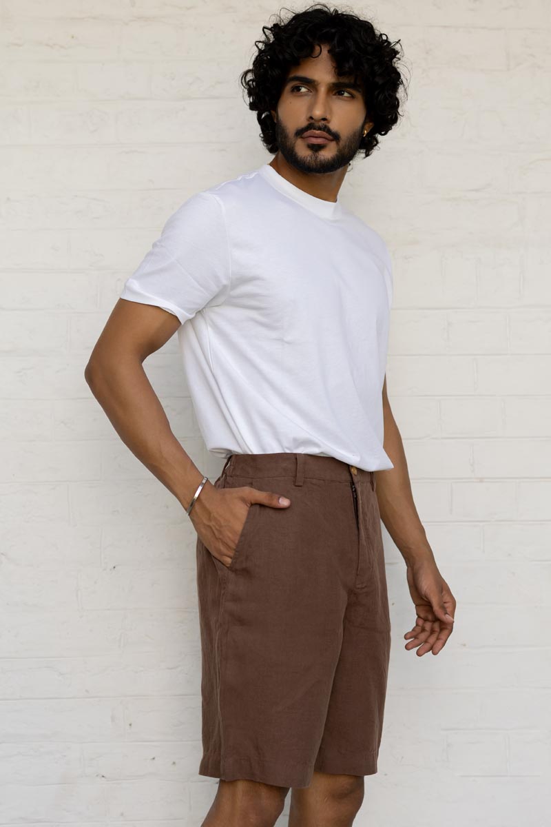 Man wearing a white t-shirt and Walnut Shorts against a white brick wall.