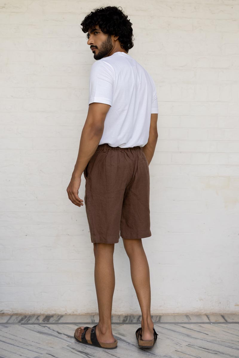 Man wearing a white t-shirt and Walnut Shorts standing against a light-colored wall.