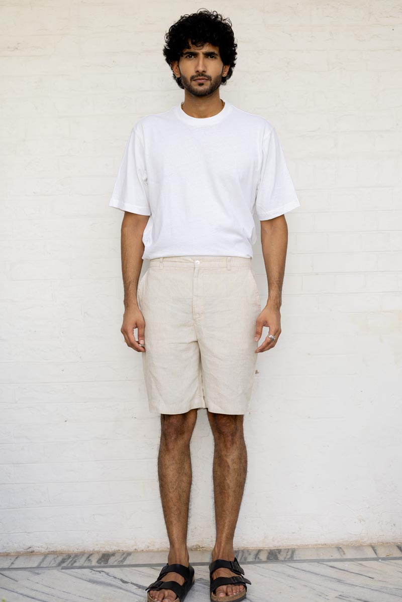 Man wearing a white t-shirt and Classic Cream Shorts against a white wall.