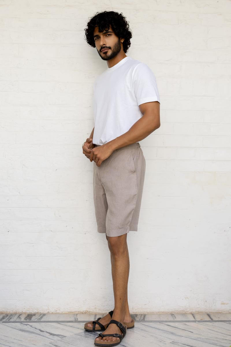 Man wearing a white t-shirt and Almond Beige Shorts standing against a white wall.