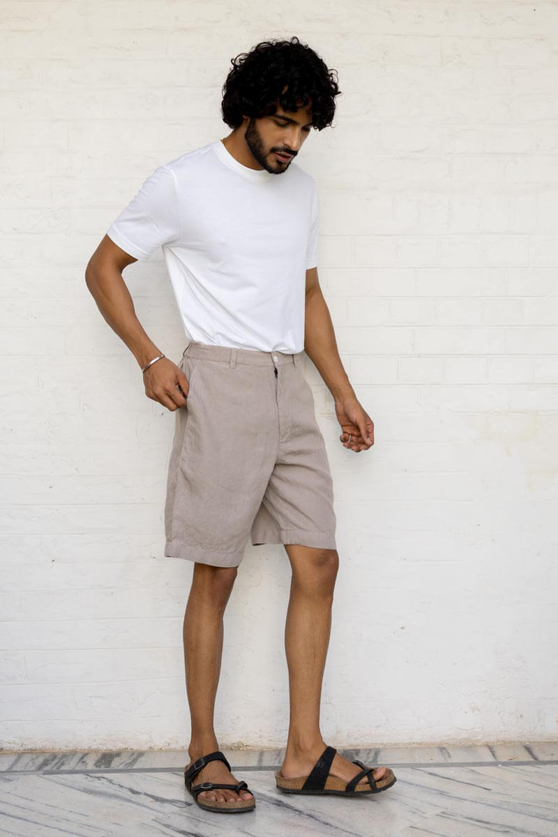 Man wearing a white t-shirt and Almond Beige Shorts against a white wall.
