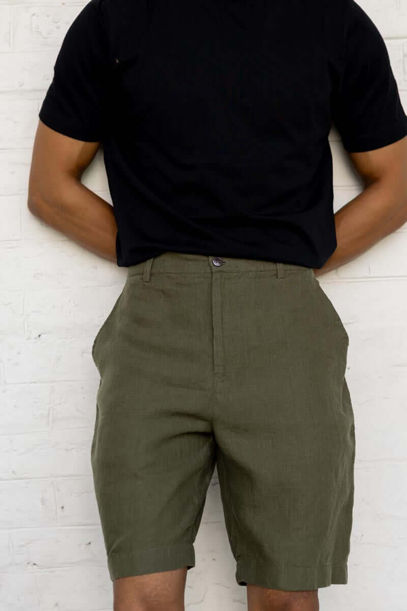 Person wearing a black t-shirt and Crocodile Green Shorts against a white brick wall.