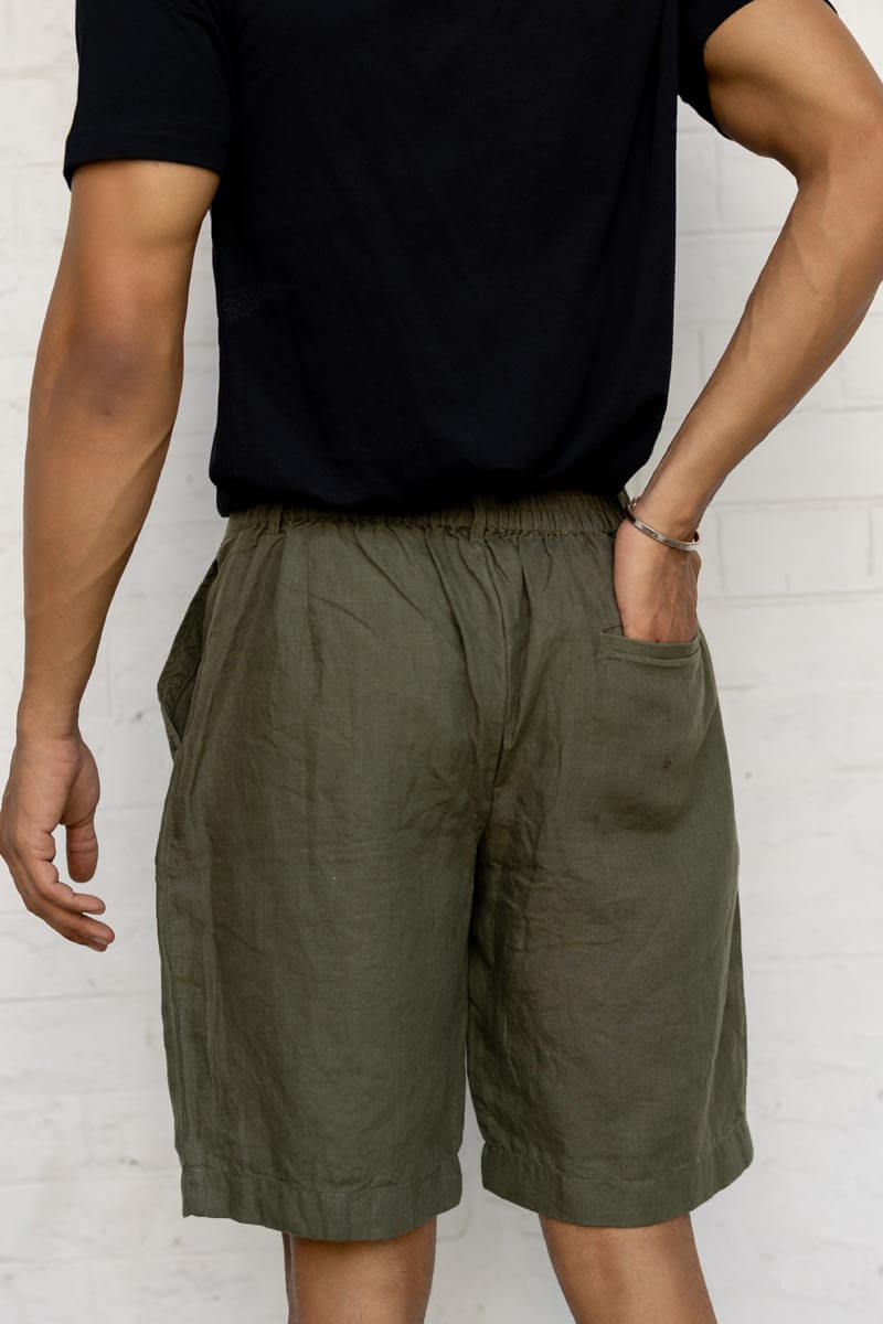 Person wearing Crocodile Green Shorts and a black shirt against a white brick wall.