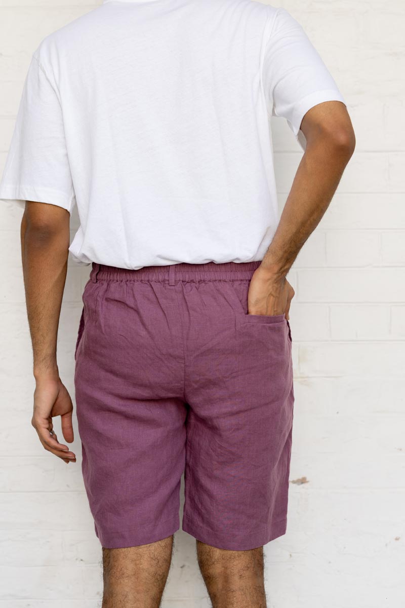 Person wearing a white t-shirt and Twilight Purple Shorts against a white brick wall.