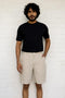 Man wearing a black t-shirt and Macadamia Shorts against a white brick wall.