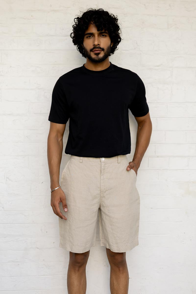 Man wearing a black t-shirt and Macadamia Shorts against a white brick wall.