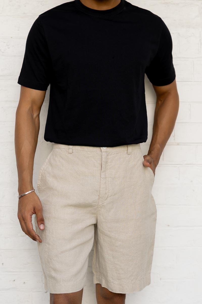 Person wearing a black t-shirt and Macadamia Shorts against a white brick wall.