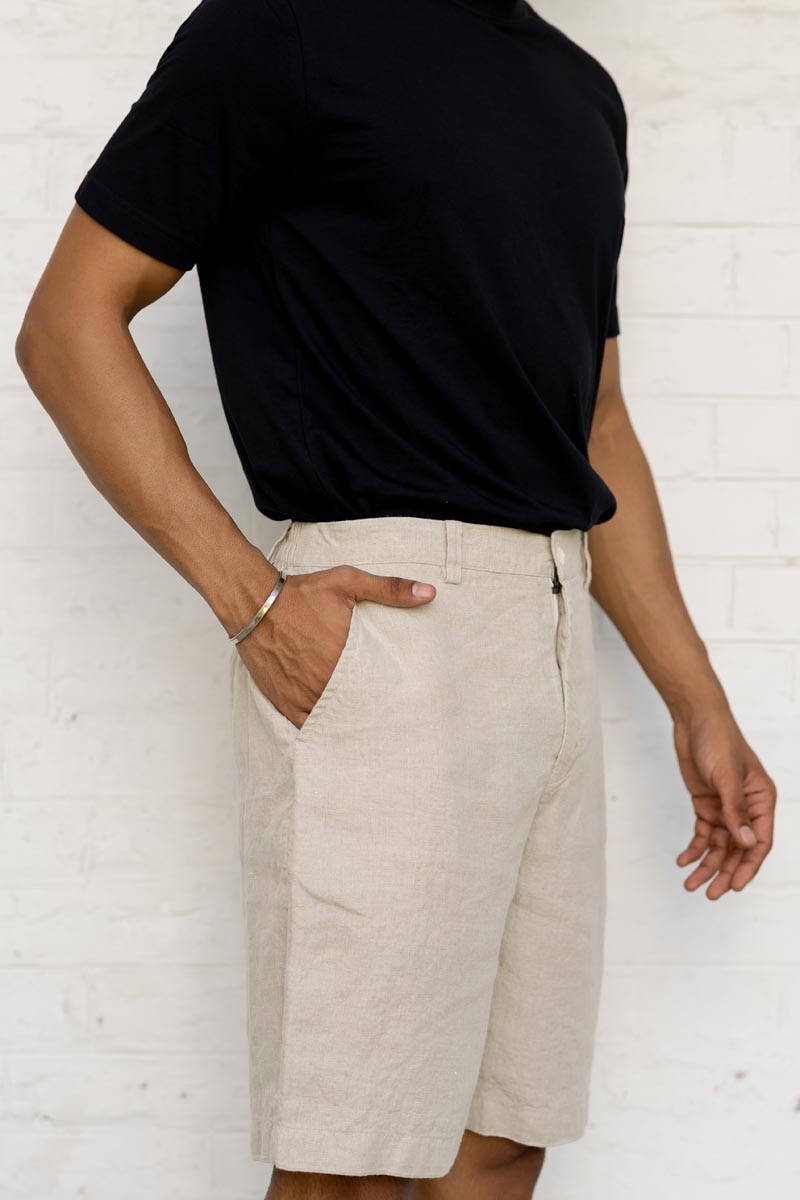 Person wearing a black t-shirt and Macadamia Shorts against a white brick wall.