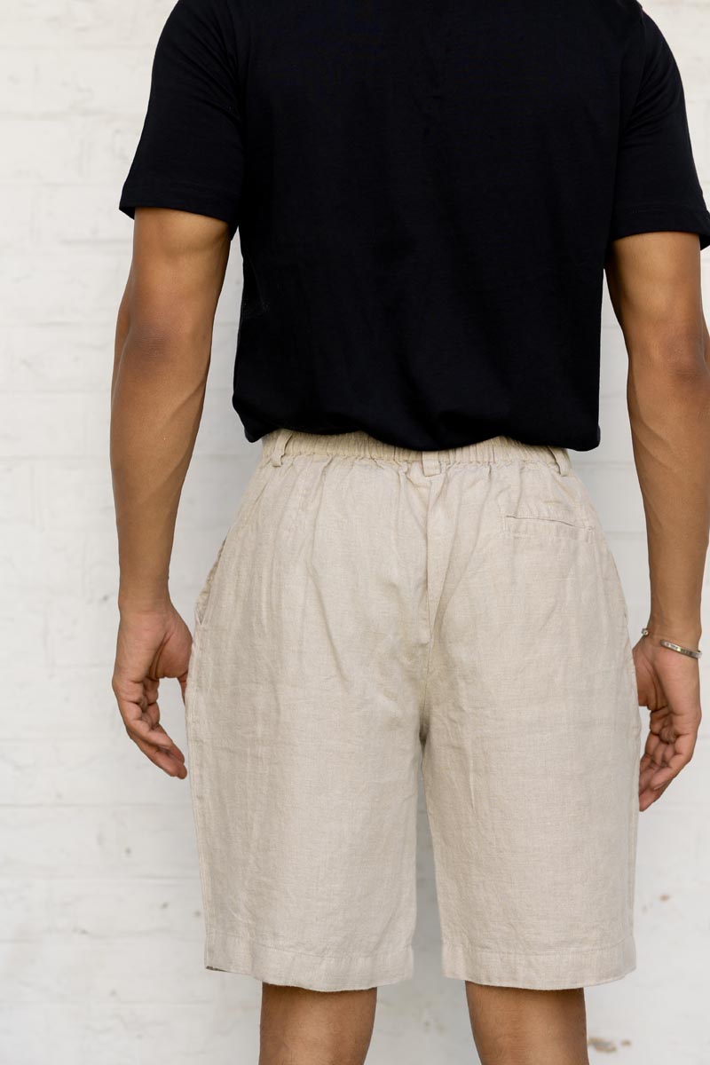 Person wearing Macadamia Shorts and a black shirt against a white brick wall.