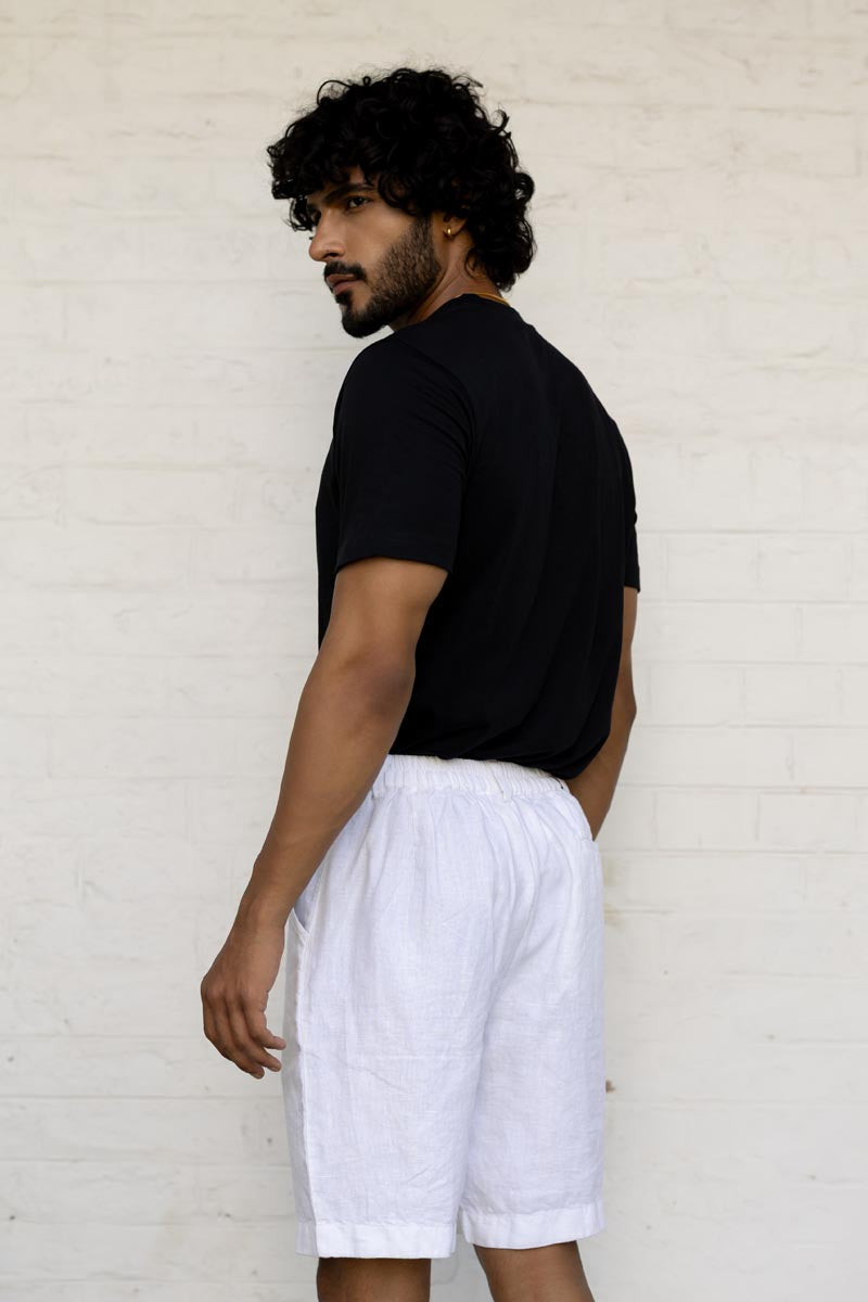Man wearing a black t-shirt and White Shorts against a light brick wall.