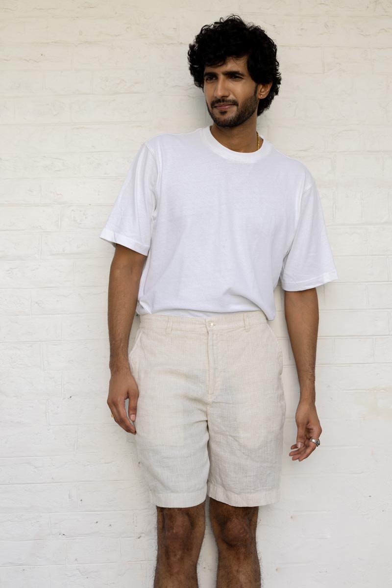 Man wearing a white t-shirt and Ivory Check Shorts against a white brick wall.