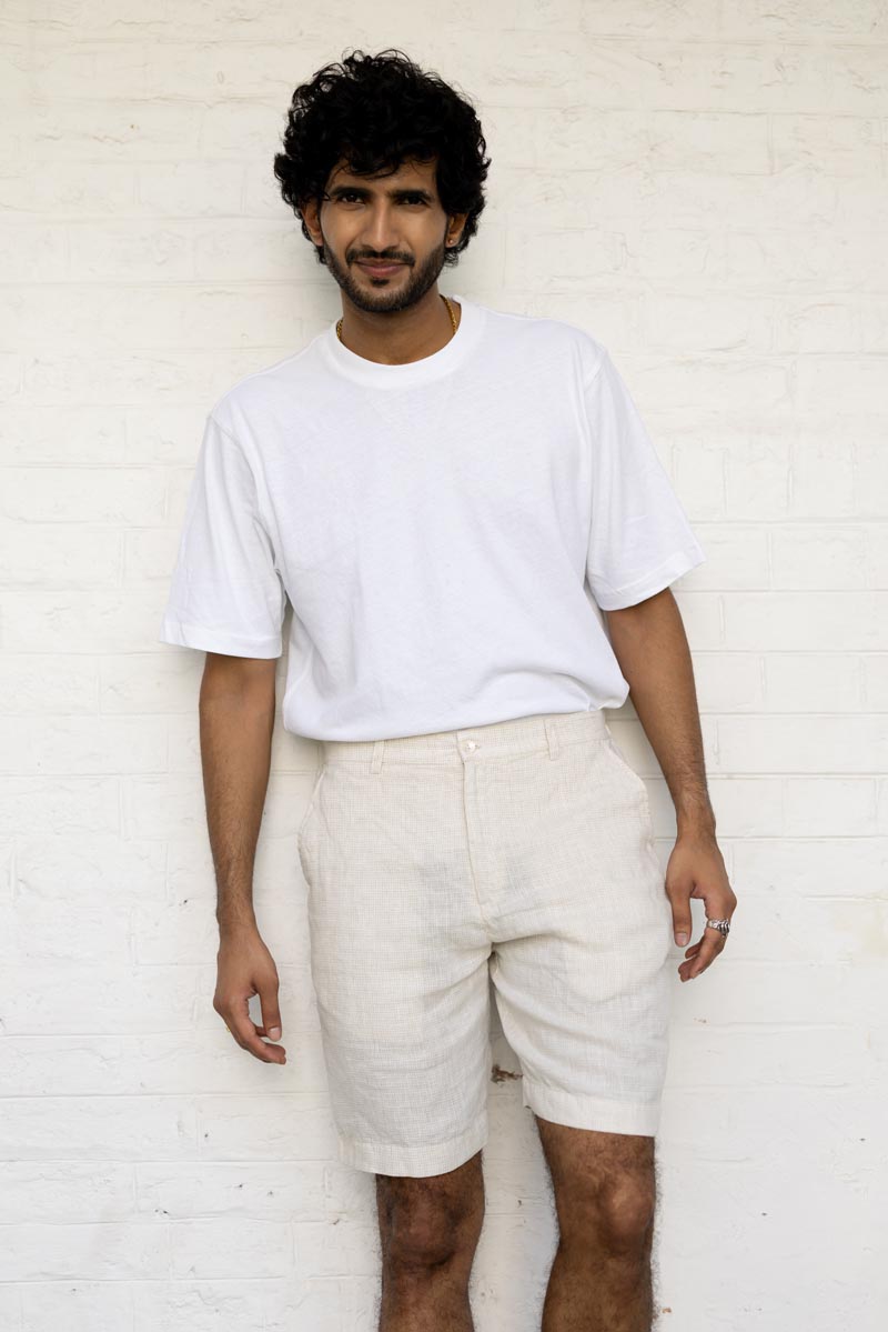 Man wearing a white t-shirt and Ivory Check Shorts against a white brick wall.