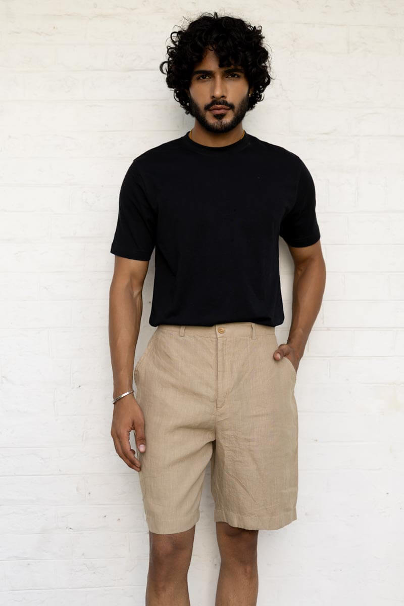 Man wearing a black t-shirt and Desert Sand Shorts against a white wall