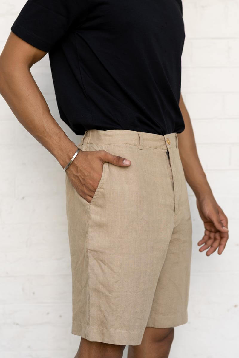 Person wearing Desert Sand Shorts and a black top against a white brick wall.