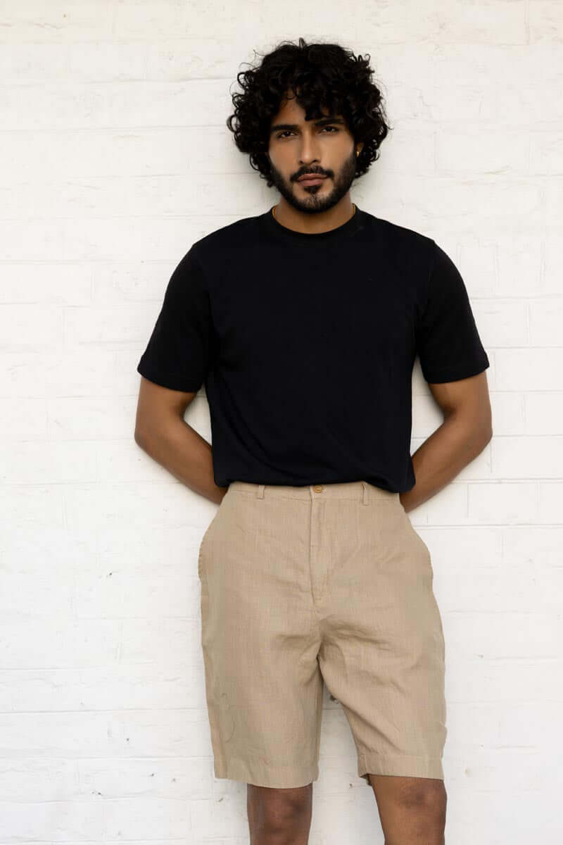 Man wearing a black t-shirt and Desert Sand Shorts against a white brick wall.