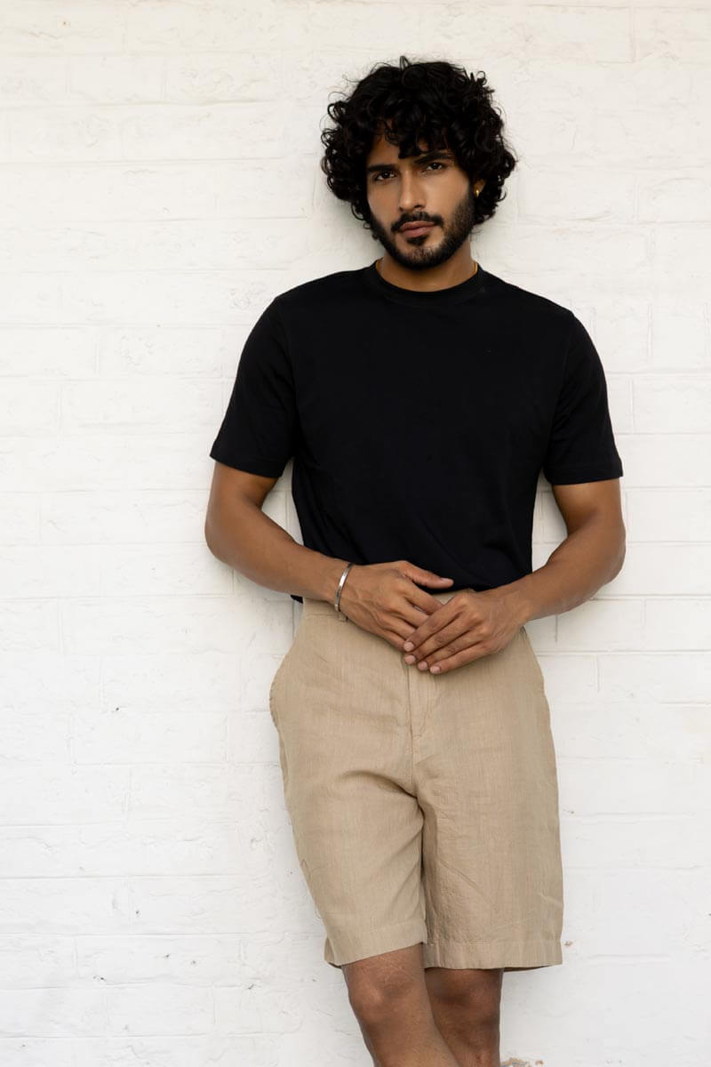 Man wearing a black t-shirt and Desert Sand Shorts against a white brick wall.