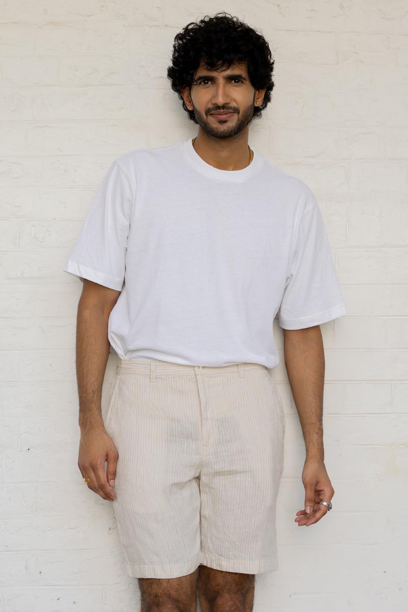 Man wearing a white t-shirt and Beige Hairline Stripe Shorts against a white brick wall.