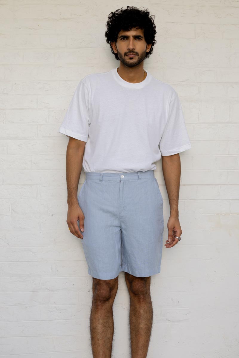 Man wearing a white t-shirt and Pacific Blue Shorts against a white brick wall.