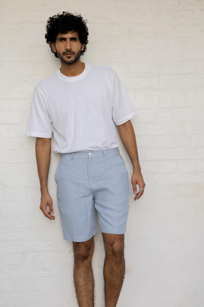Man wearing a white t-shirt and Pacific Blue Shorts against a white brick wall.