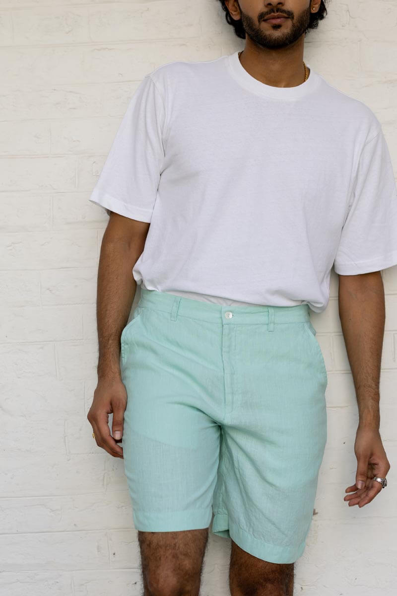 Person wearing a white t-shirt and Celestial Green Shorts against a white brick wall.