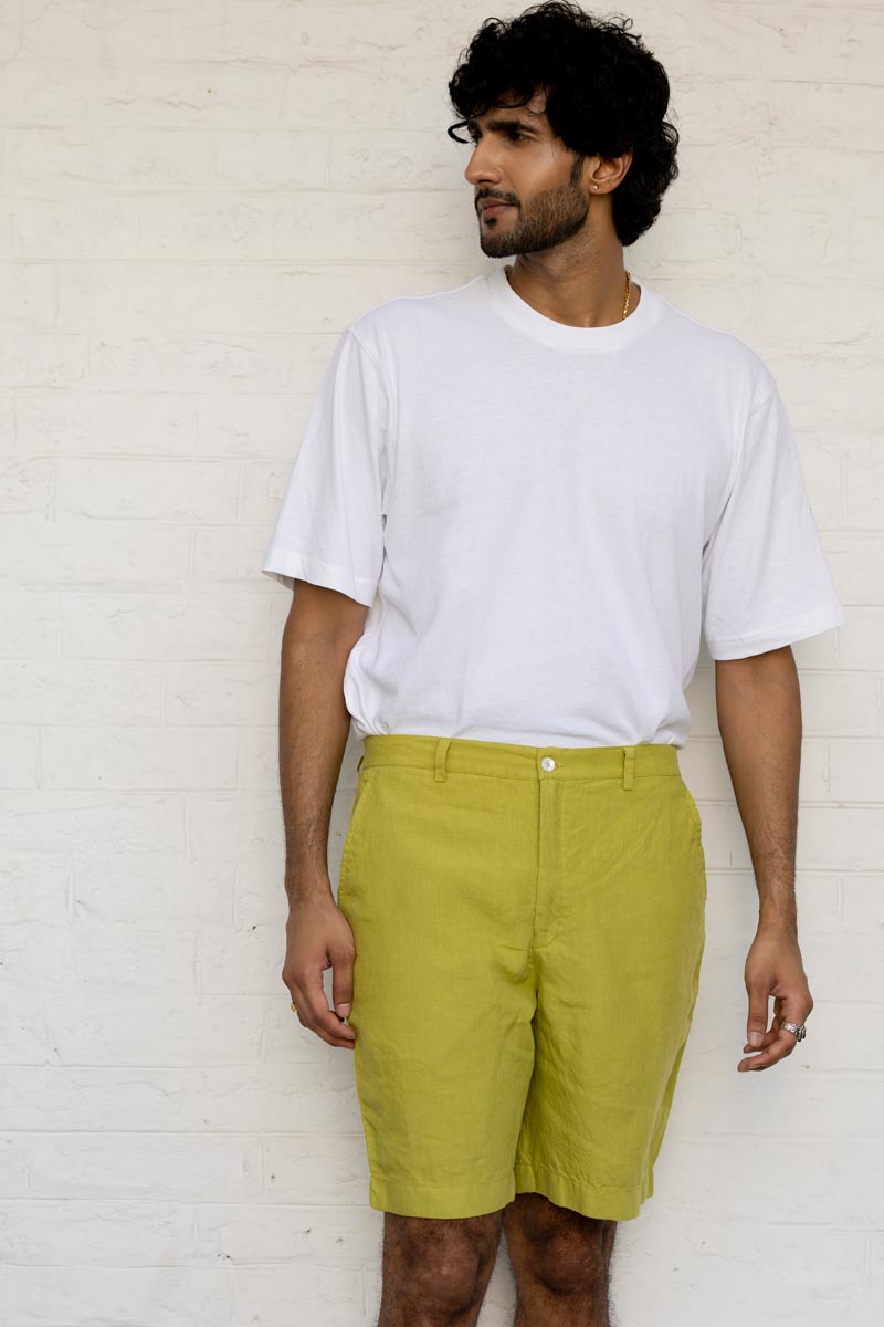 Man wearing a white t-shirt and Kiwi Green Shorts against a white brick wall.