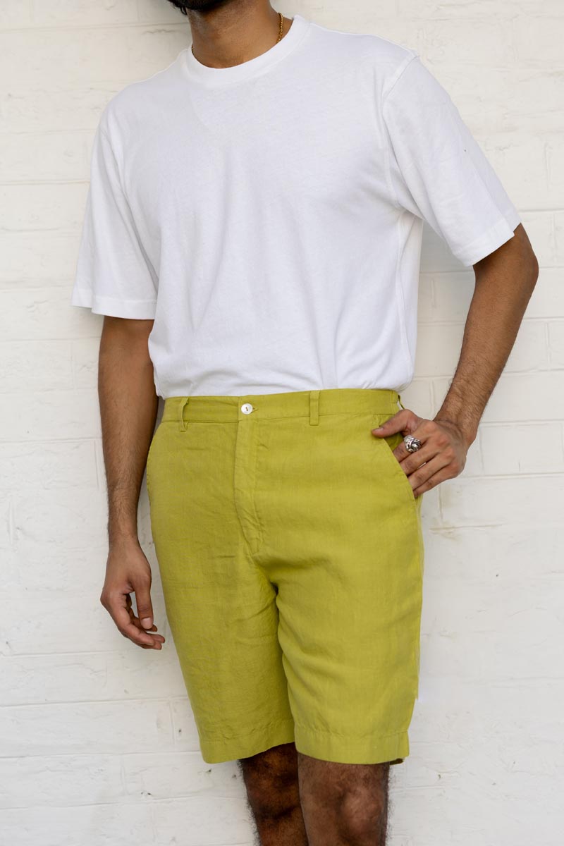 Person wearing a white t-shirt and Kiwi Green Shorts against a white brick wall.