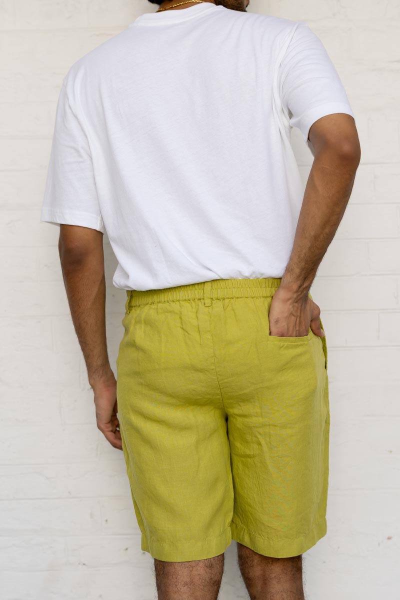 Person wearing a white t-shirt and Kiwi Green Shorts against a white brick wall.