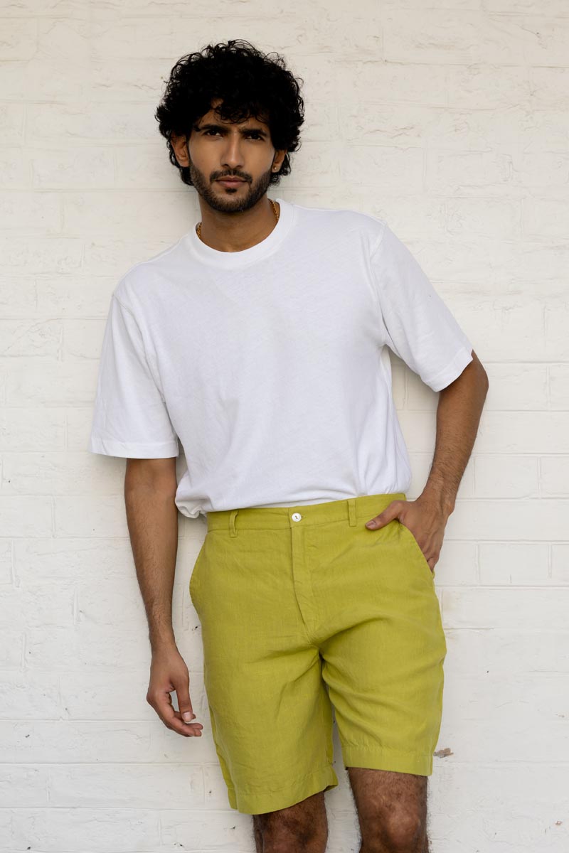 Man wearing a white t-shirt and Kiwi Green Shorts against a white brick wall.