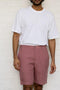 Person wearing a white t-shirt and Rose Gold Shorts against a white brick wall.