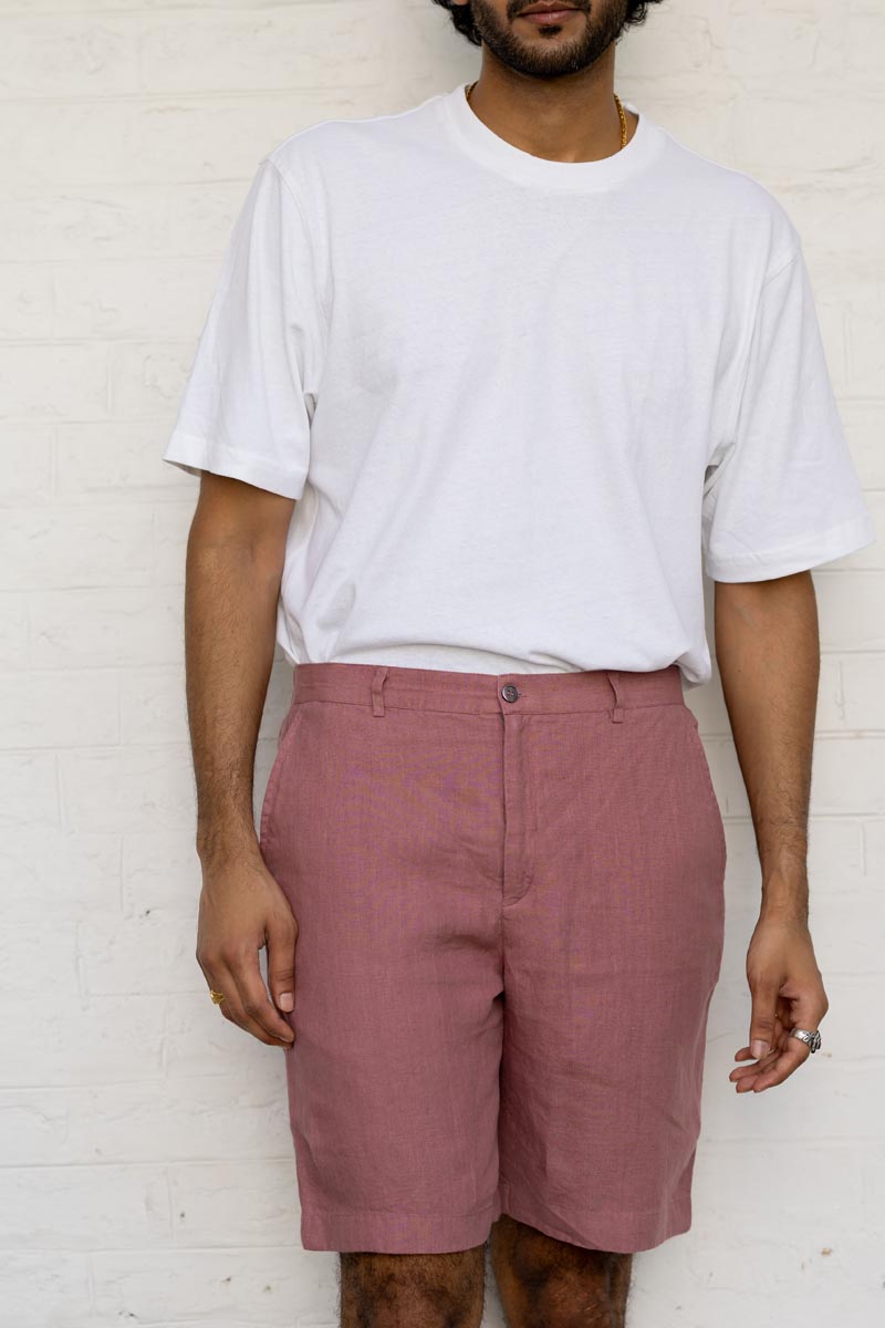 Person wearing a white t-shirt and Rose Gold Shorts against a white brick wall.