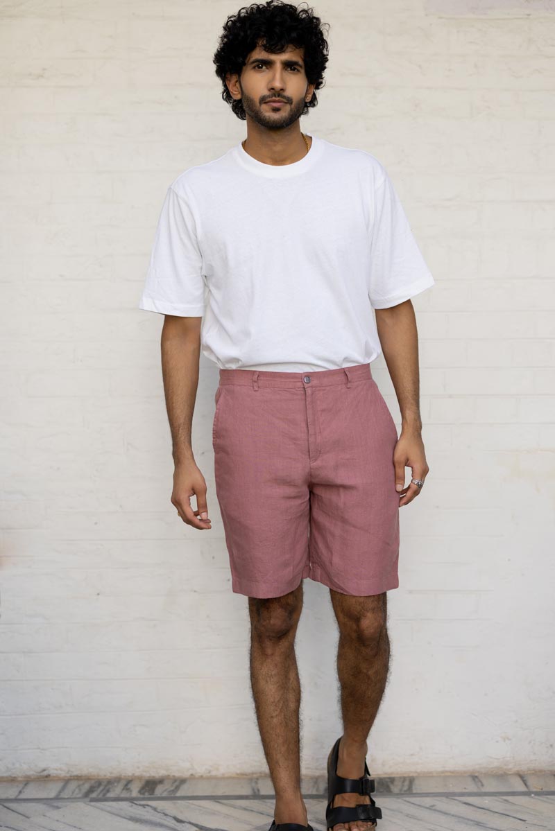 Man wearing a white t-shirt and Rose Gold Shorts against a light-colored wall.